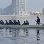 Dragon boat team paddling in Sharjah with city skyline in the background