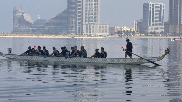 Dragon boat team paddling in Sharjah with city skyline in the background