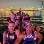 Desert Falcons dragon boat team paddling together on Deira Creek under evening city lights.
