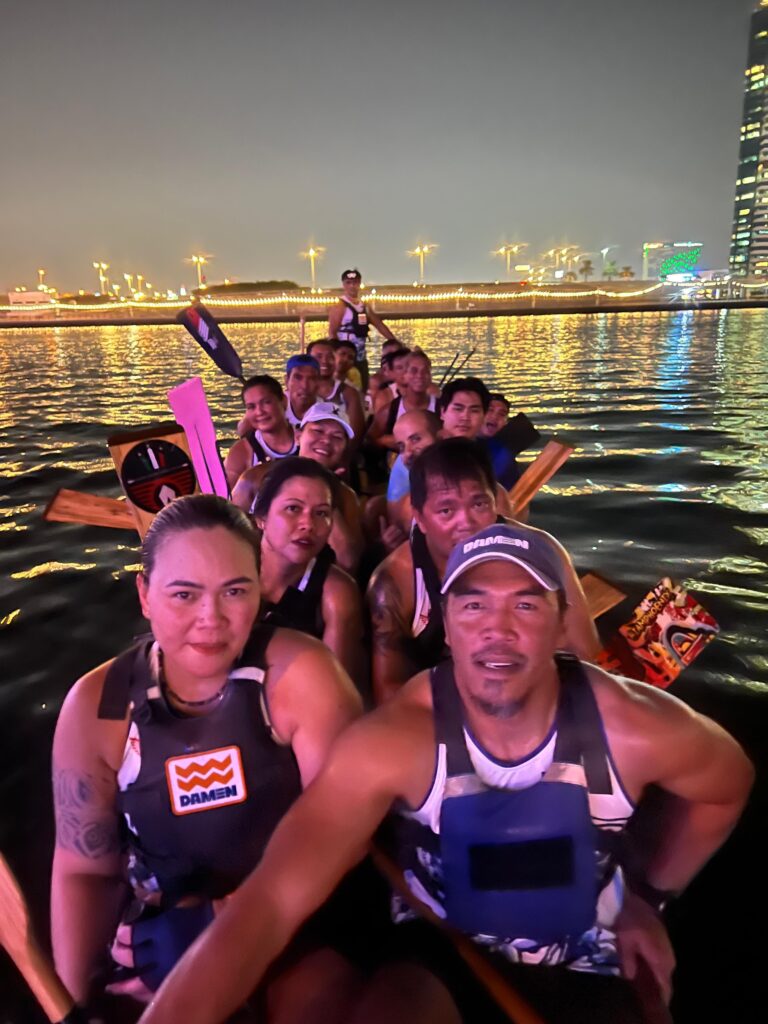 Desert Falcons dragon boat team paddling together on Deira Creek under evening city lights.